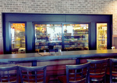 bar counter with chairs in front and wall of glass coolers behind